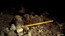 a yellow stick is laying on a pile of rocks in a dark area
