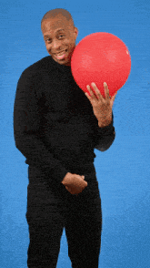 a man in a black sweater is holding a red balloon in front of his face