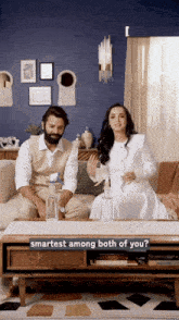 a man and a woman sitting on a couch with a sign that says " smartest among both of you "