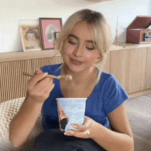 a woman in a blue shirt is eating from a cup that says van loon