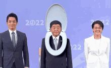 a man in a suit with a toilet seat on his head stands next to two other people .