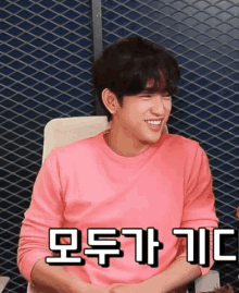 a man in a pink shirt is smiling in front of a metal mesh wall