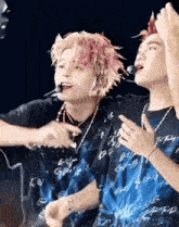 a couple of men are standing next to each other on a stage . one of the men has pink hair .