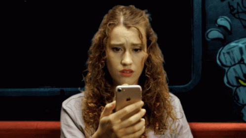 a woman with curly hair is looking at her phone and making a face