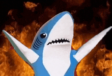 a blue and white stuffed shark with its arms outstretched is standing in front of a fire .