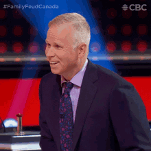 a man in a suit and tie is smiling in front of a sign that says family feud canada