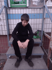 a young boy sits on a set of stairs in front of a green atm machine
