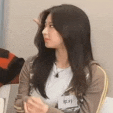 a woman with long black hair is sitting at a table with her hands folded and looking at the camera .
