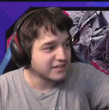 a young man wearing headphones and a grey shirt is sitting in front of a computer screen .
