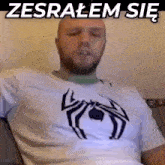 a man wearing a white shirt with a black spider on it