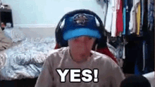 a man wearing headphones and a baseball cap is sitting in front of a camera and says yes .