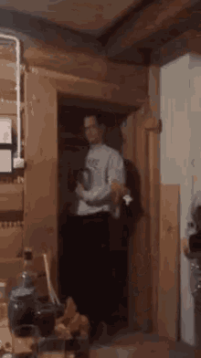 a man is standing in a doorway in a wooden room holding a dog .