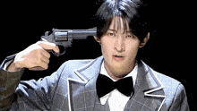a young man in a suit and bow tie is holding a gun to his head .