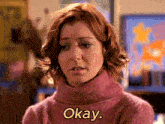 a woman in a pink sweater says okay in yellow letters