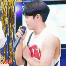 a young man is singing into a microphone while wearing a white tank top .