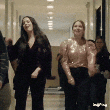 a group of women are dancing in a hallway and one of them is wearing a pink top .