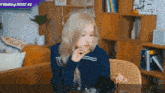 a woman with blonde hair is sitting at a table in a living room with a sign that says making rose # 2 .