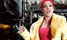 a woman with pink hair is wearing a yellow coat and a pink tank top .