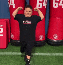 a young boy is flexing his muscles on a football field in front of a row of red dummies .