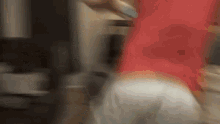 a person in a red shirt and white shorts is standing in a kitchen .