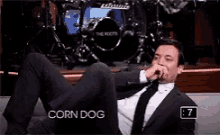 a man in a suit and tie is sitting on a couch with his legs crossed and covering his nose with his hand .
