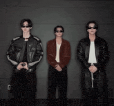 three men wearing sunglasses and leather jackets are standing next to each other .