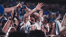 a crowd of people are gathered in a stadium and one of them is screaming with his hands in the air