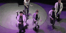 a group of people in lab coats are dancing in a circle on a stage