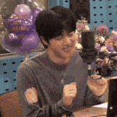 a man sitting in front of a microphone with purple balloons behind him that say welcome to our street