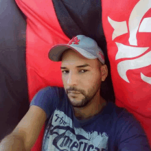 a man wearing a hat and a t-shirt is taking a selfie in front of a flag .