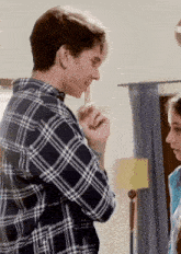 a man in a plaid shirt covering his mouth with his hand