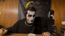 a man with face paint sitting at a table next to a can of zo