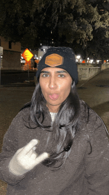 a woman wearing a black beanie and gloves is making a funny face and giving the middle finger