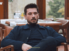 a man with a beard is sitting in a chair with his legs crossed and the words minimalmoons visible in the corner