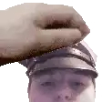 a hand is putting something on a man 's head while wearing a hat .
