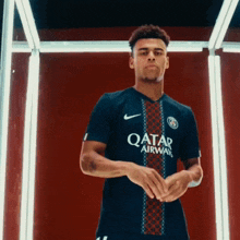 a man in a qatar airways jersey stands in front of a red background