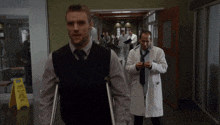 a man with crutches is walking down a hallway next to a caution sign