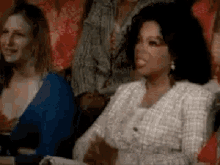 oprah winfrey is sitting in front of a crowd of people and smiling .