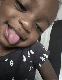 a little girl sticking her tongue out and wearing a black shirt with white letters on it