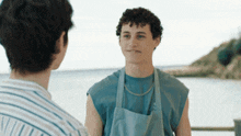 a young man wearing an apron talks to another young man