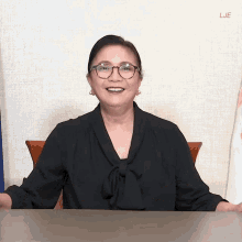 a woman wearing glasses and a black shirt is smiling in front of a wall with the letters lje on it