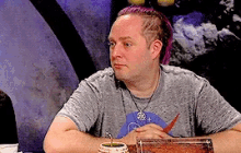 a man with purple hair is sitting at a table with a drink in front of him