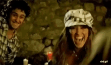 a man and a woman are sitting at a table and laughing . the woman is wearing a hat and smiling .
