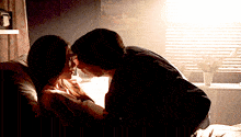 a man and a woman kissing in front of a window with blinds