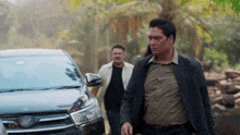 a man in a suit is walking next to a car .