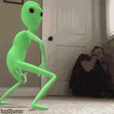 a green alien is dancing in front of a door while a man takes a picture .