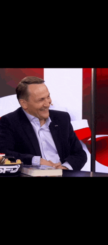 a man in a suit is smiling while sitting at a table with a book in front of him .
