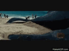 a whale is laying on a sandy beach with people walking by