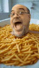 a bald man with glasses is laying in a bowl of french fries