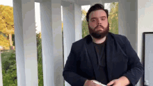 a man with a beard is standing in front of a balcony holding a cell phone .